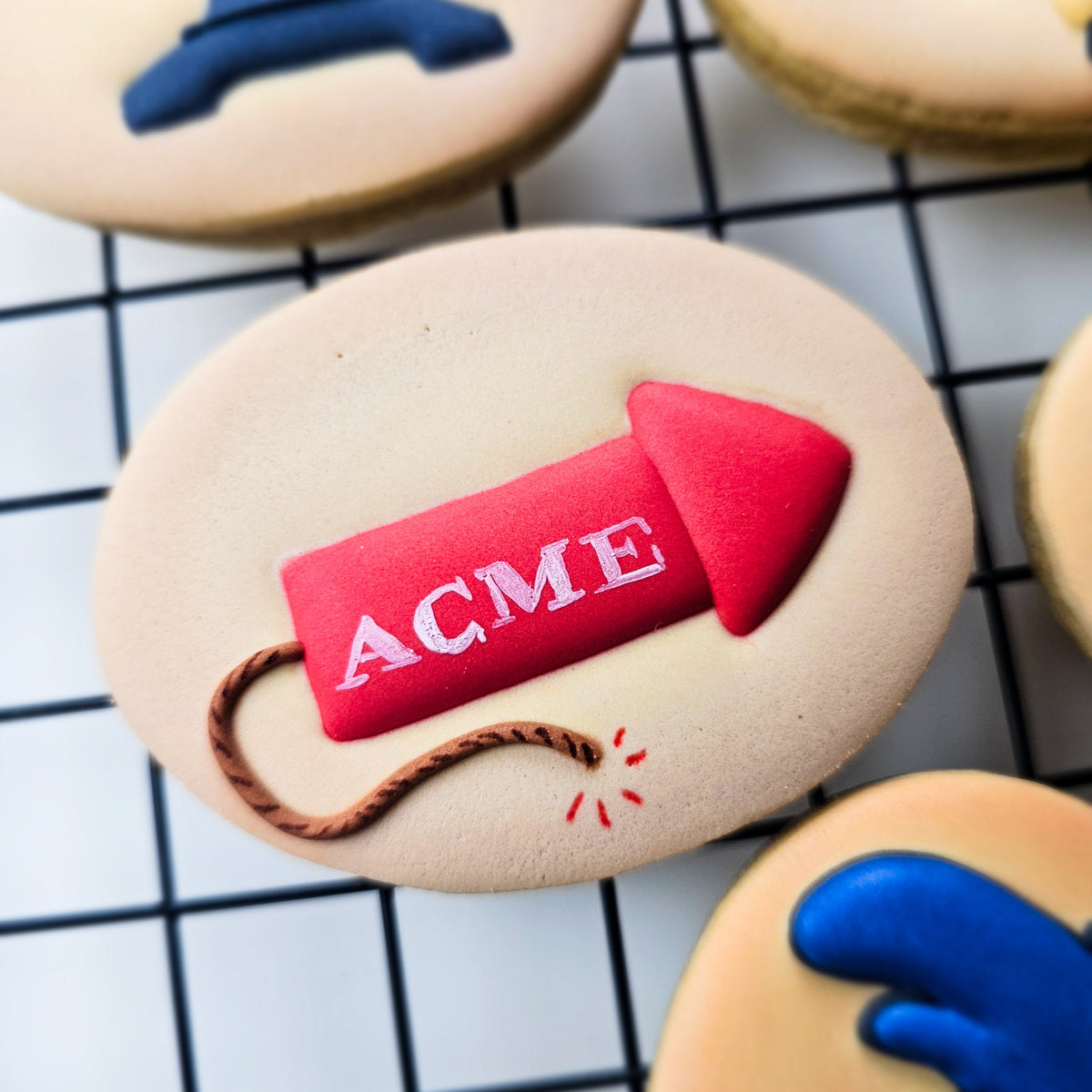 Red Acme rocket royal icing transfer on a tan oval shaped decorated sugar cookie sitting on a black grid