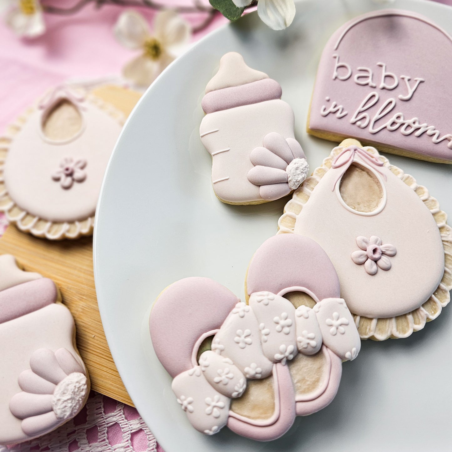 Baby shoes, a bottle, a bib, and baby in bloom sugar cookies on a white plate