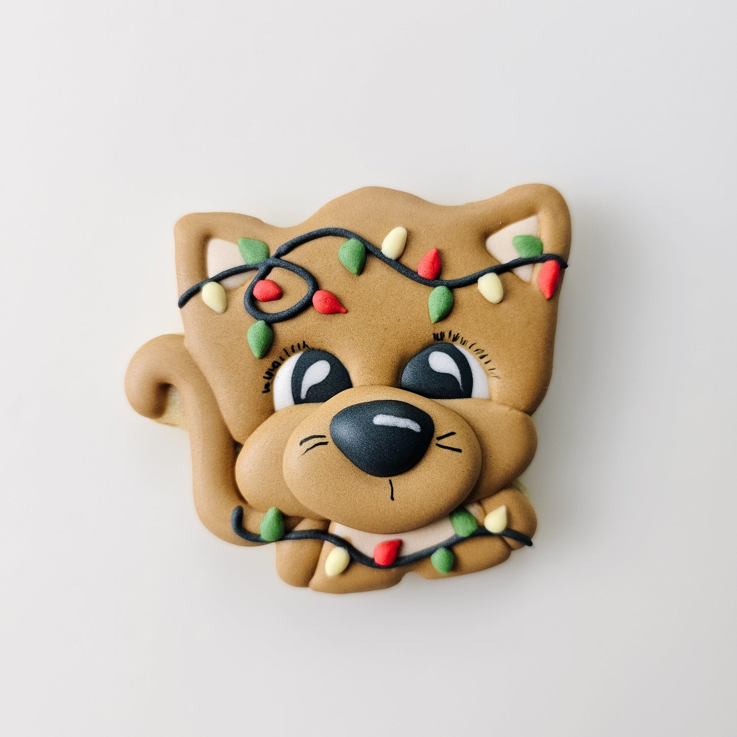 An adorable Christmas cat sugar cookie tangled up in Christmas lights on a light gray background