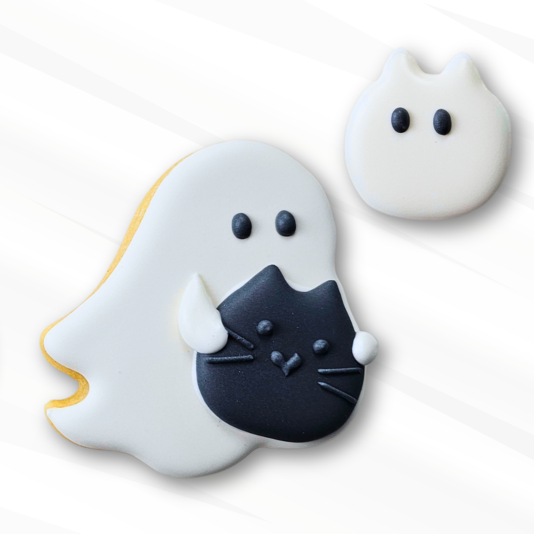 Cute ghost-shaped sugar cookie decorated with icing, one large white ghost cookie holding a black cat royal icing tra, and one white ghost cat royal icing transfer, set against a clean white background with soft diagonal shadows.