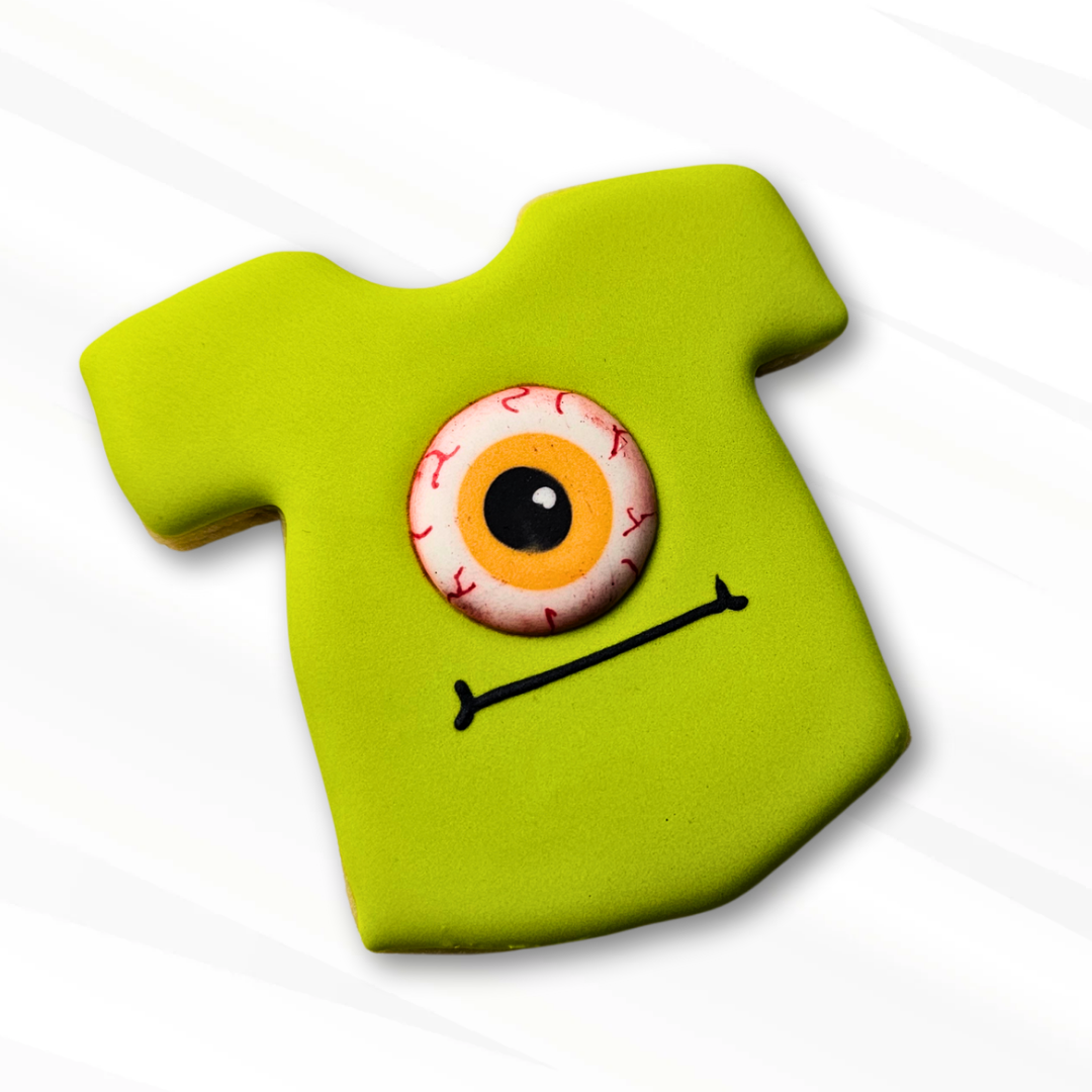 Green T-shirt sugar cookie with a spooky bloodshot eyeball royal icing transfer monster design on a white background