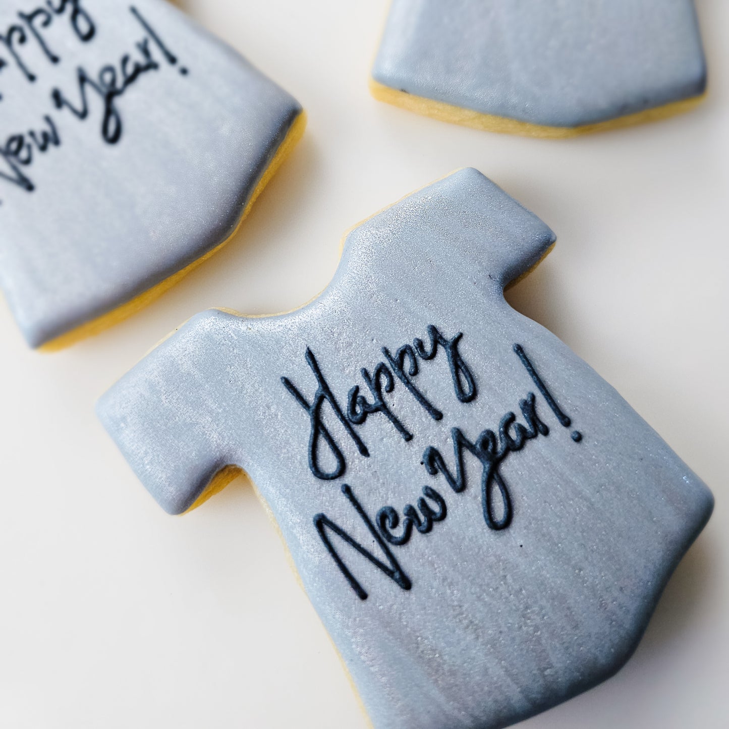 Decorated sugar cookie shaped like a T-shirt with 'Happy New Year!' text on a white background