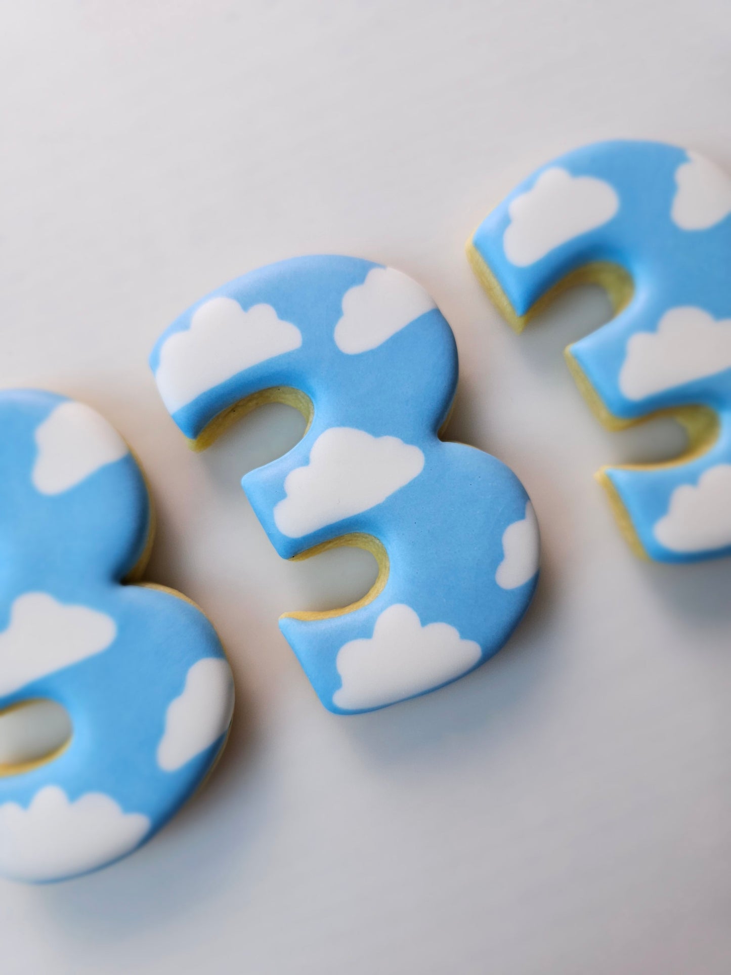 Decorative number 3 sugar cookies iced with clouds and blue sky on a light gray background