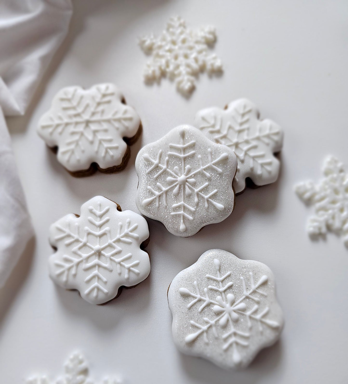 White snowflake sugar cookies on a white plate with decorative snowflakes around.