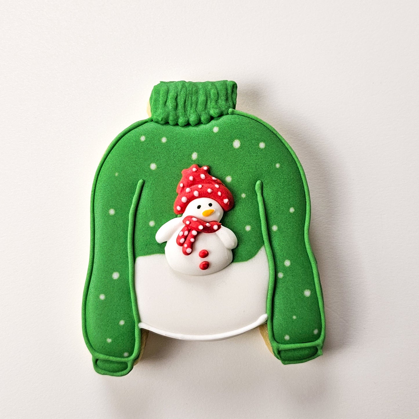 Sugar Cookie decorated like a green sweater with a snowman on a white background