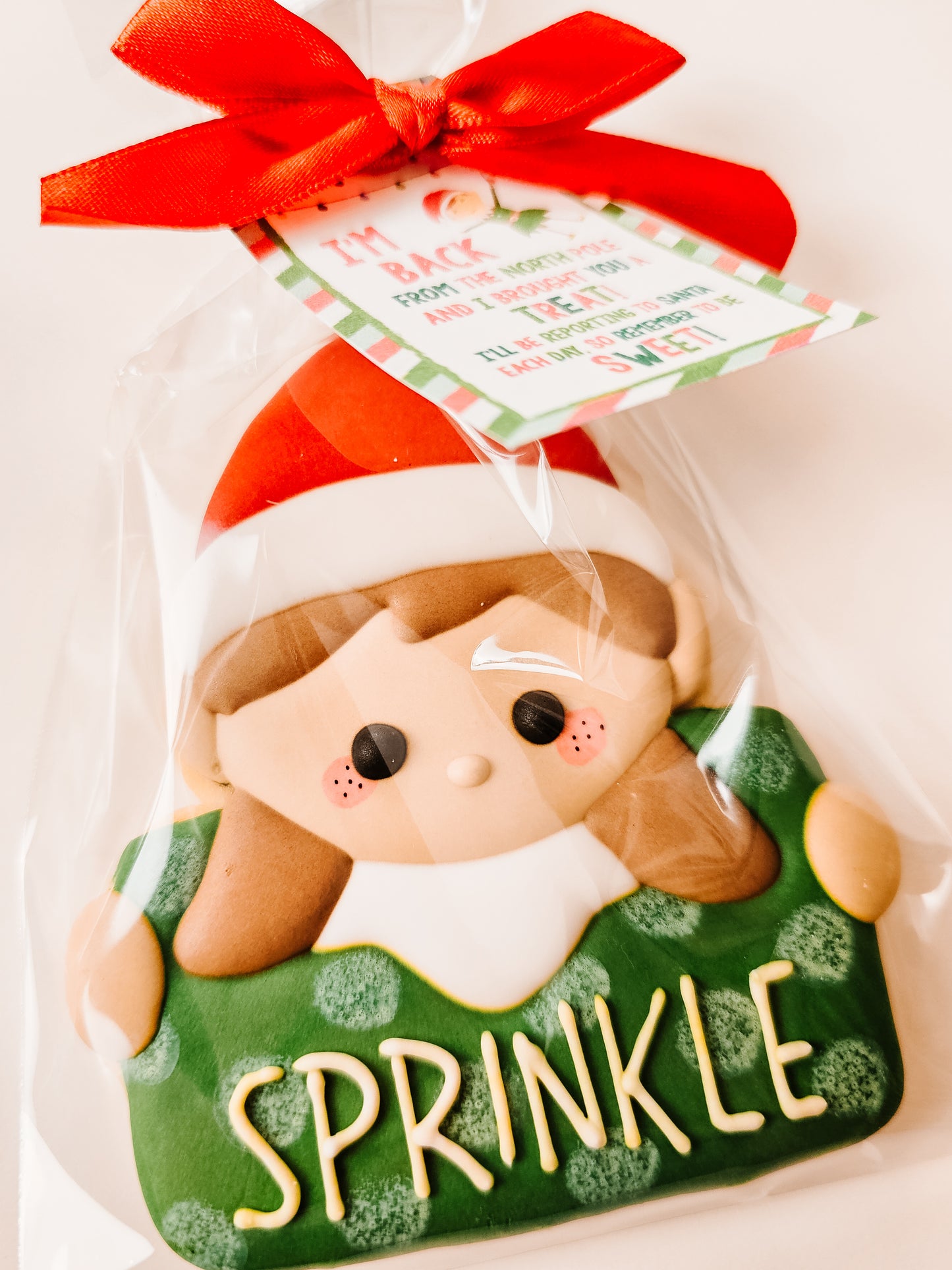 Decorative sugar cookie shaped like a girl elf with a red bow and 'Sprinkle' text on a white background