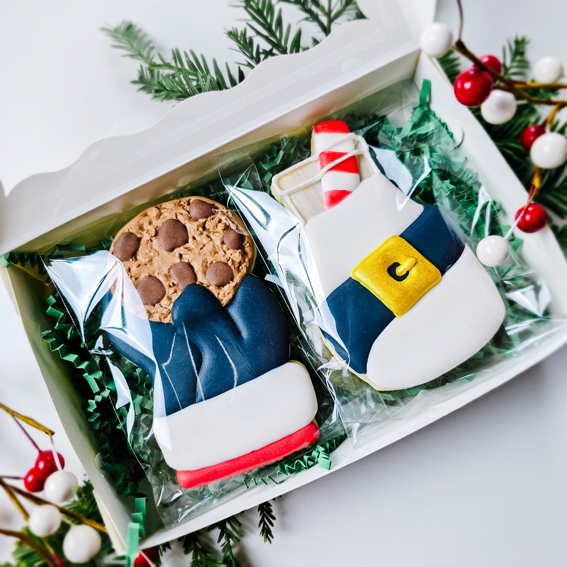 A decorated Christmas cookie of Santa holding a chocolate chip cookie and a bottle of milk with Santa's belt around it