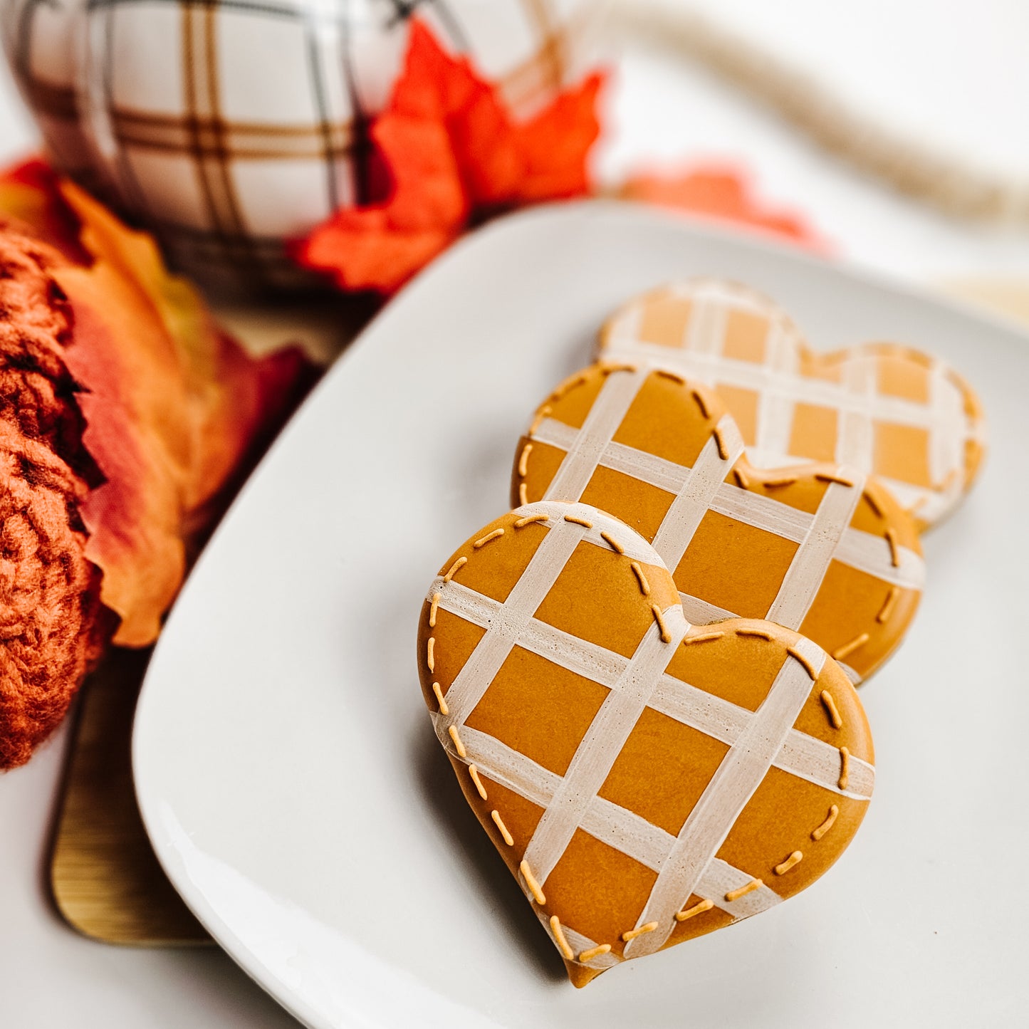 Heart-shaped sugar cookies with plqie design on a white plate, surrounded by autumn-themed decor.