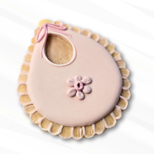 Pink baby bib sugar cookie with a flower design on a white background