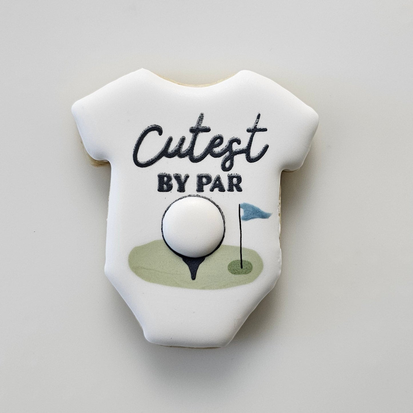 Baby onesie sugar cookie with 'Cutest by Par' text and golf ball design on a light gray background
