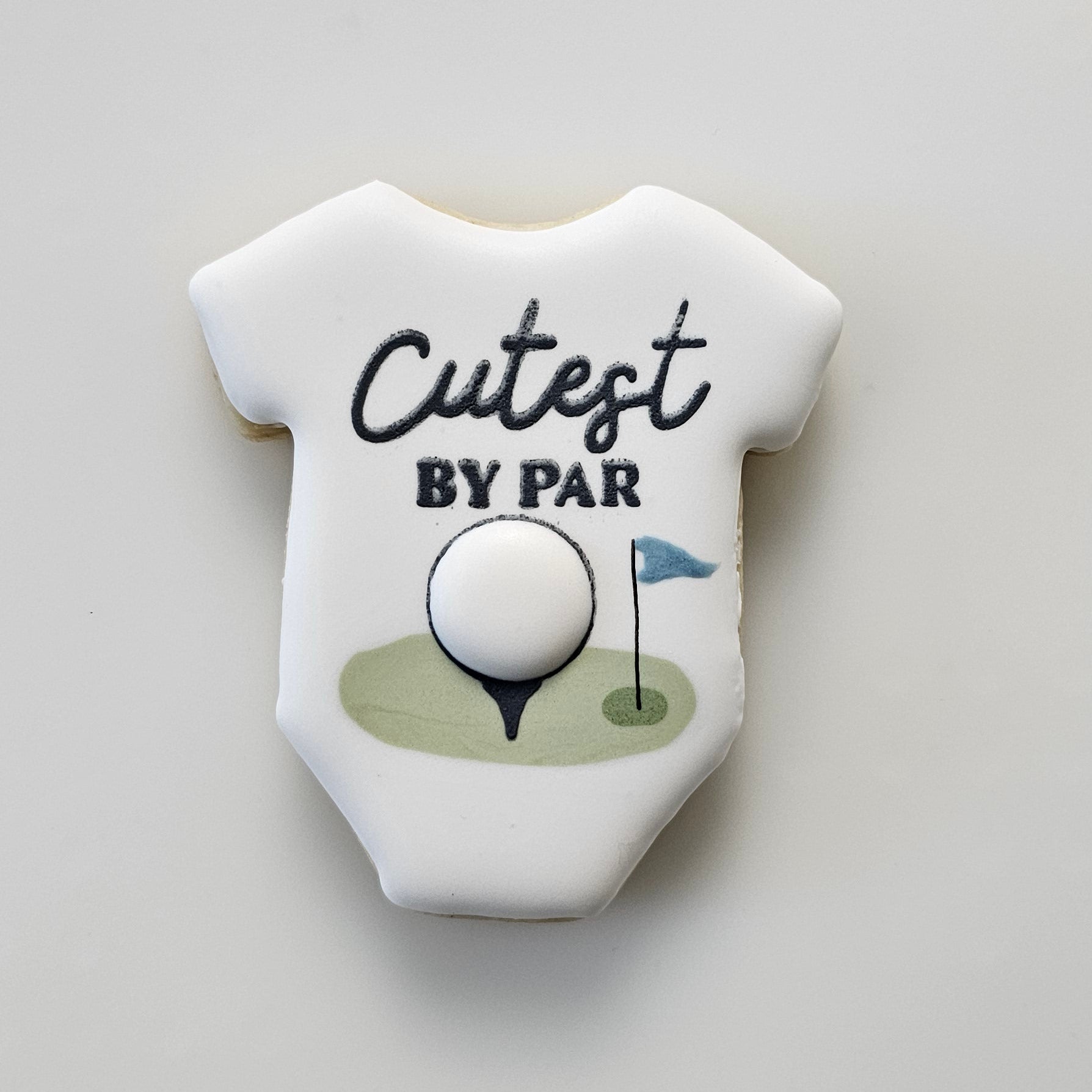 Baby onesie sugar cookie with 'Cutest by Par' text and golf ball design on a light gray background