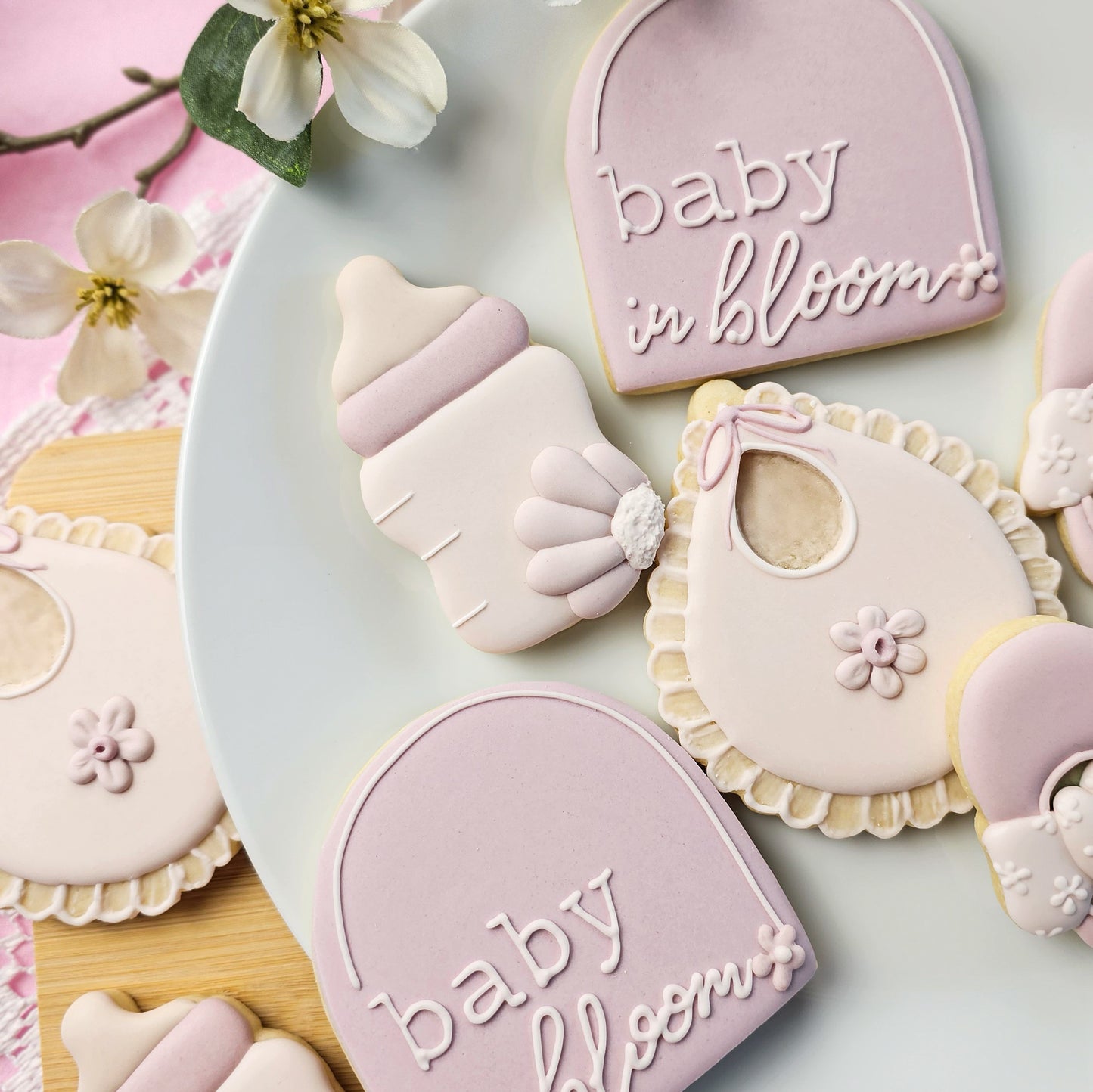 Decorative sugar cookies shaped like a baby bottle, bib, and a plaque with 'baby in bloom' text on a light background.