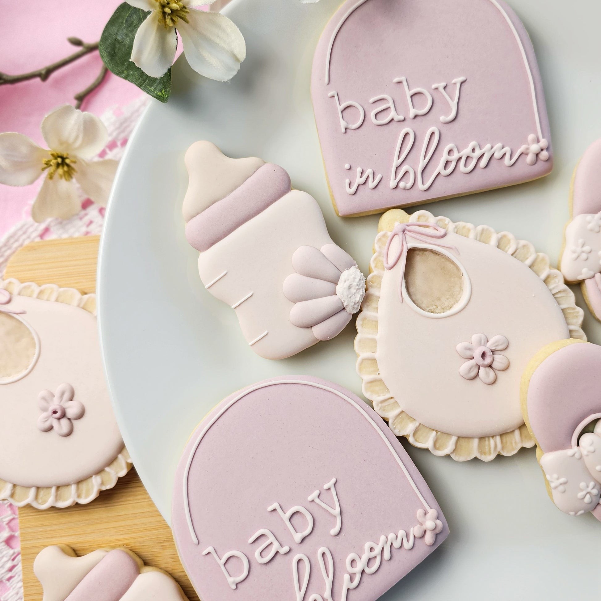 Decorative sugar cookies shaped like a baby bottle, bib, and a plaque with 'baby in bloom' text on a light background.