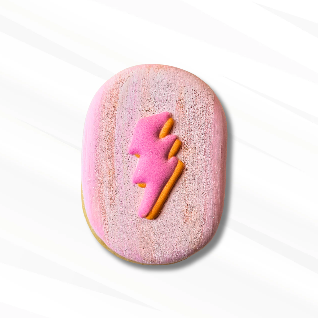 A capsule-shaped pink frosted sugar cookie with a pink and orange lightning-bolt design on top, centered on a white background with soft diagonal shadows.