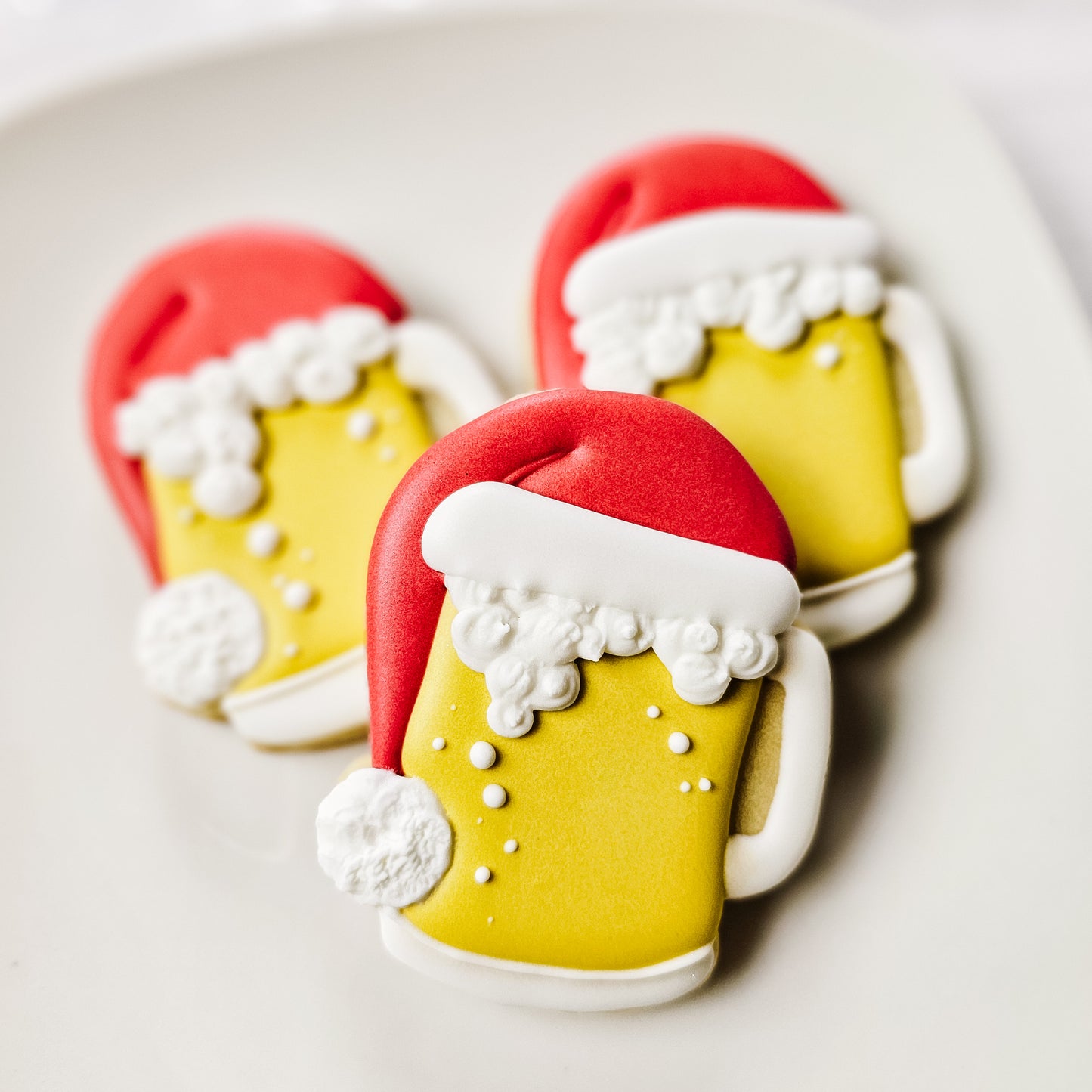Three sugar cookies of beer mugs with Santa hats on a white plate.