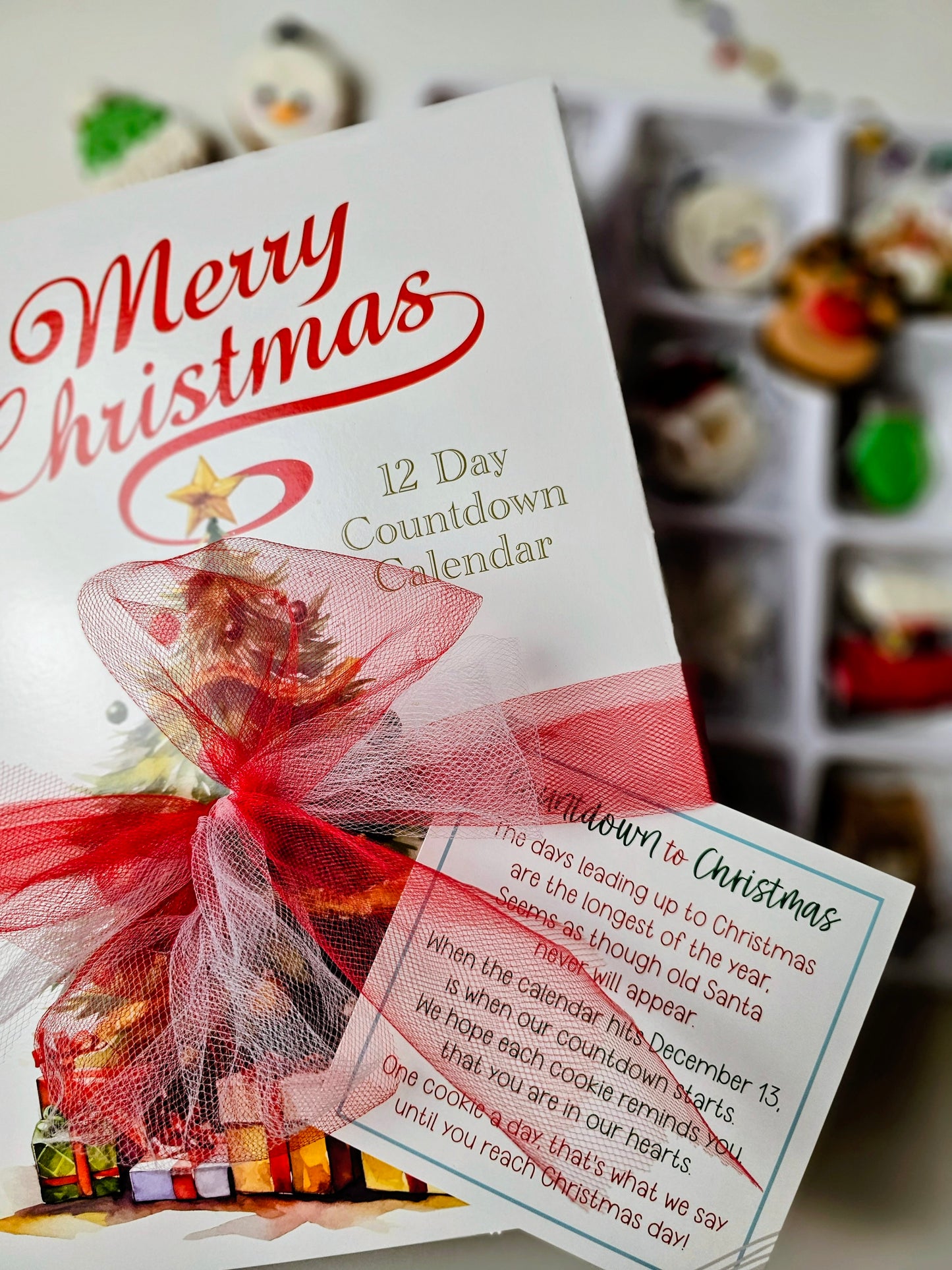 Merry Christmas 12 Day cookie Countdown Calendar with red ribbon and blurred gift boxes in the background