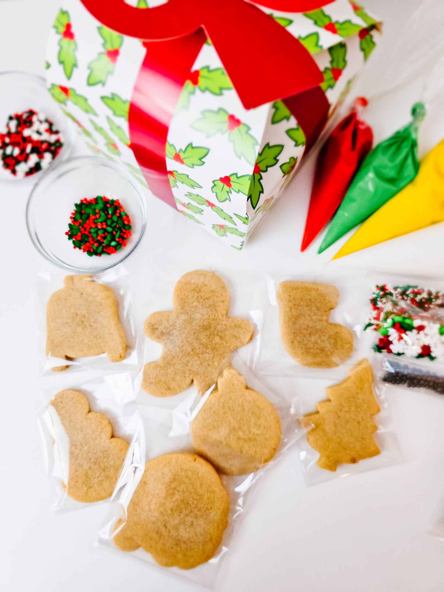 Decorative Christmas-themed sugar cookie DIY kit with icing and sprinkles on a white surface