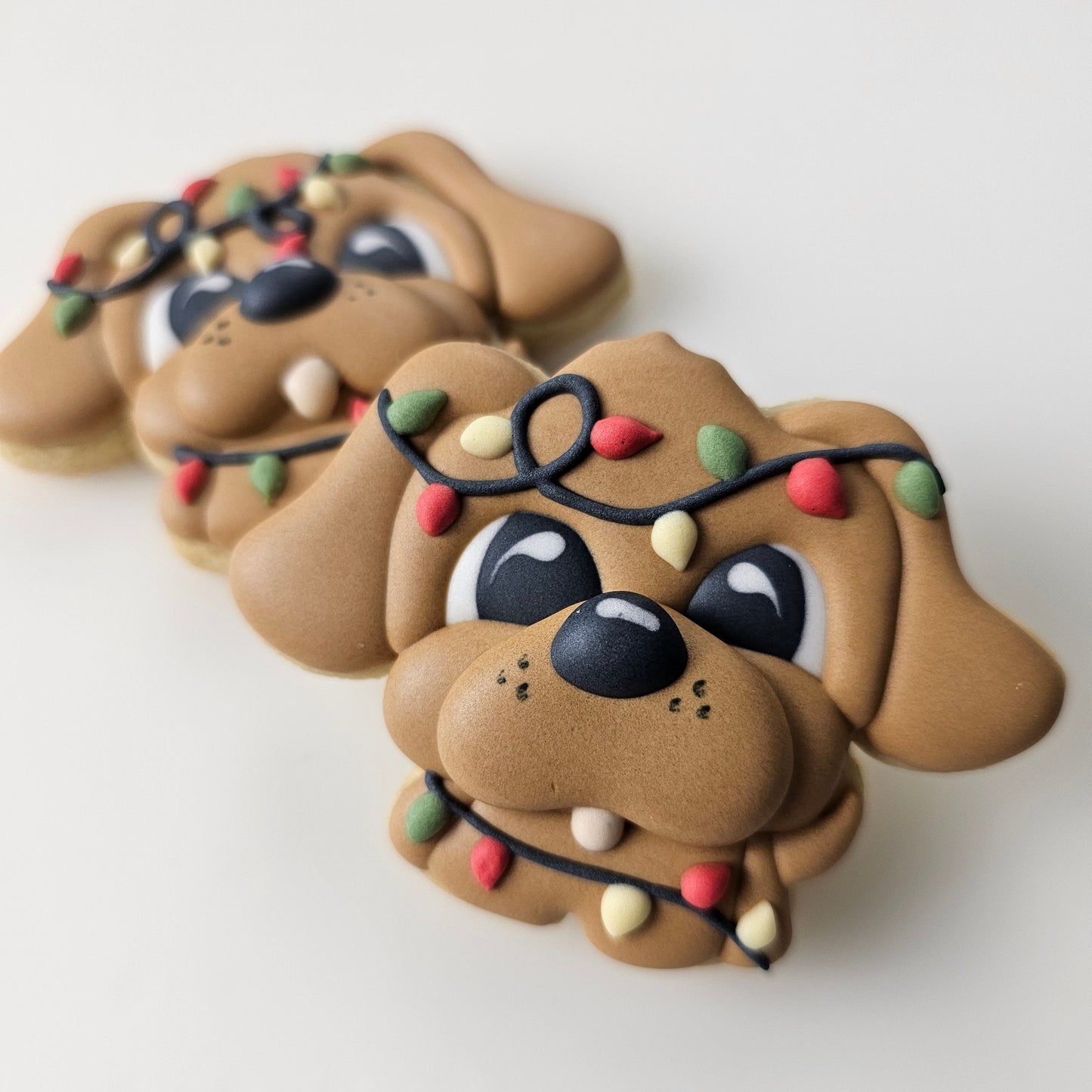 An adorable puppy dog sugar cookie tangled up in Christmas lights on a light gray background