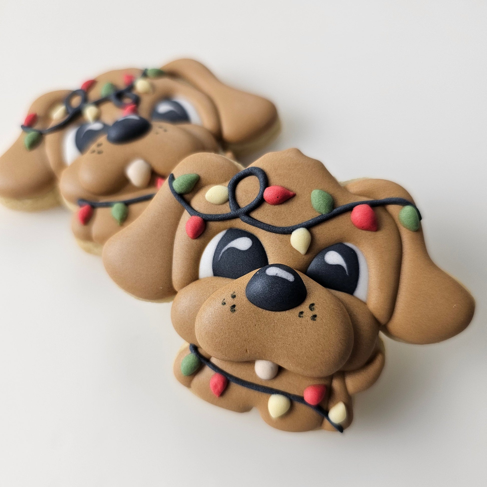 An adorable puppy dog sugar cookie tangled up in Christmas lights on a light gray background