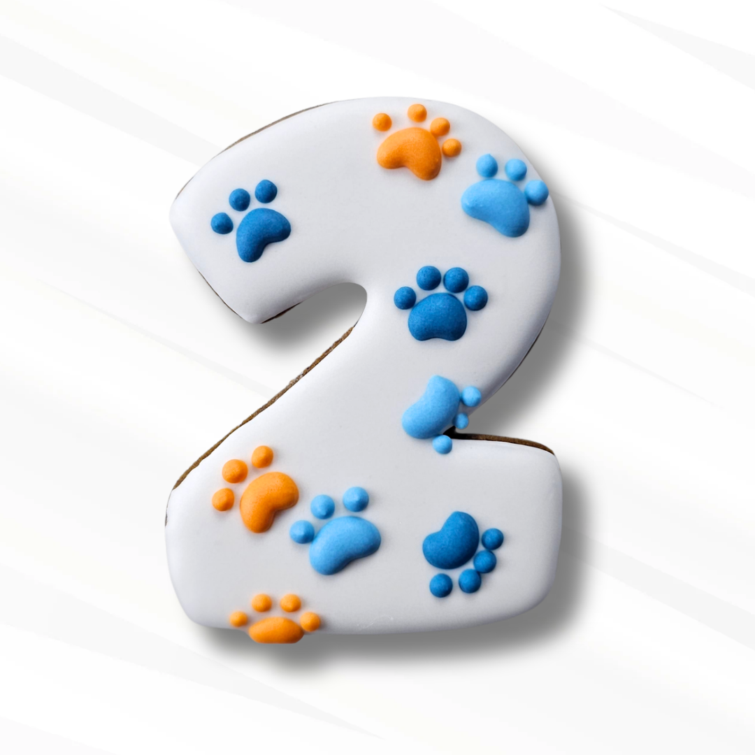 A number 2 shaped sugar cookie decorated with white icing and blue and orange paw prints, shown on a clean white background.
