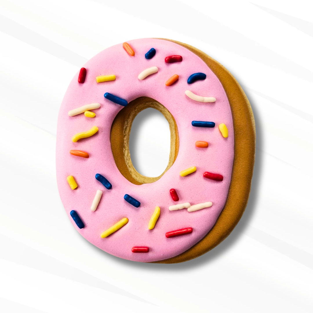 A number 0 sugar cookie decorated to look like a donut with pink frosting, multicolored sprinkles, and a golden-brown base, shown on a clean white background.