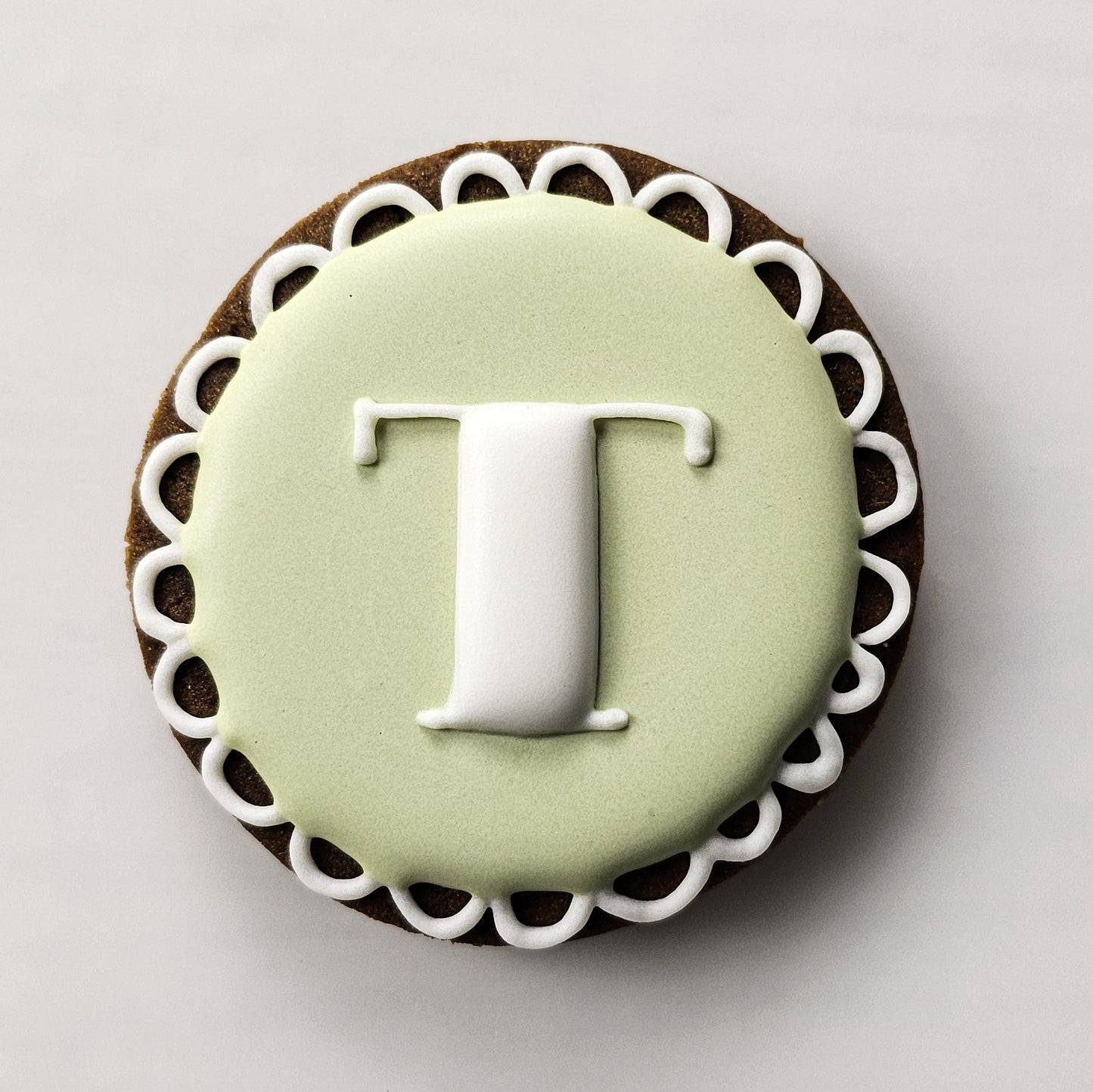 Sugar cookie with green icing and white letter 'T' on a light gray background