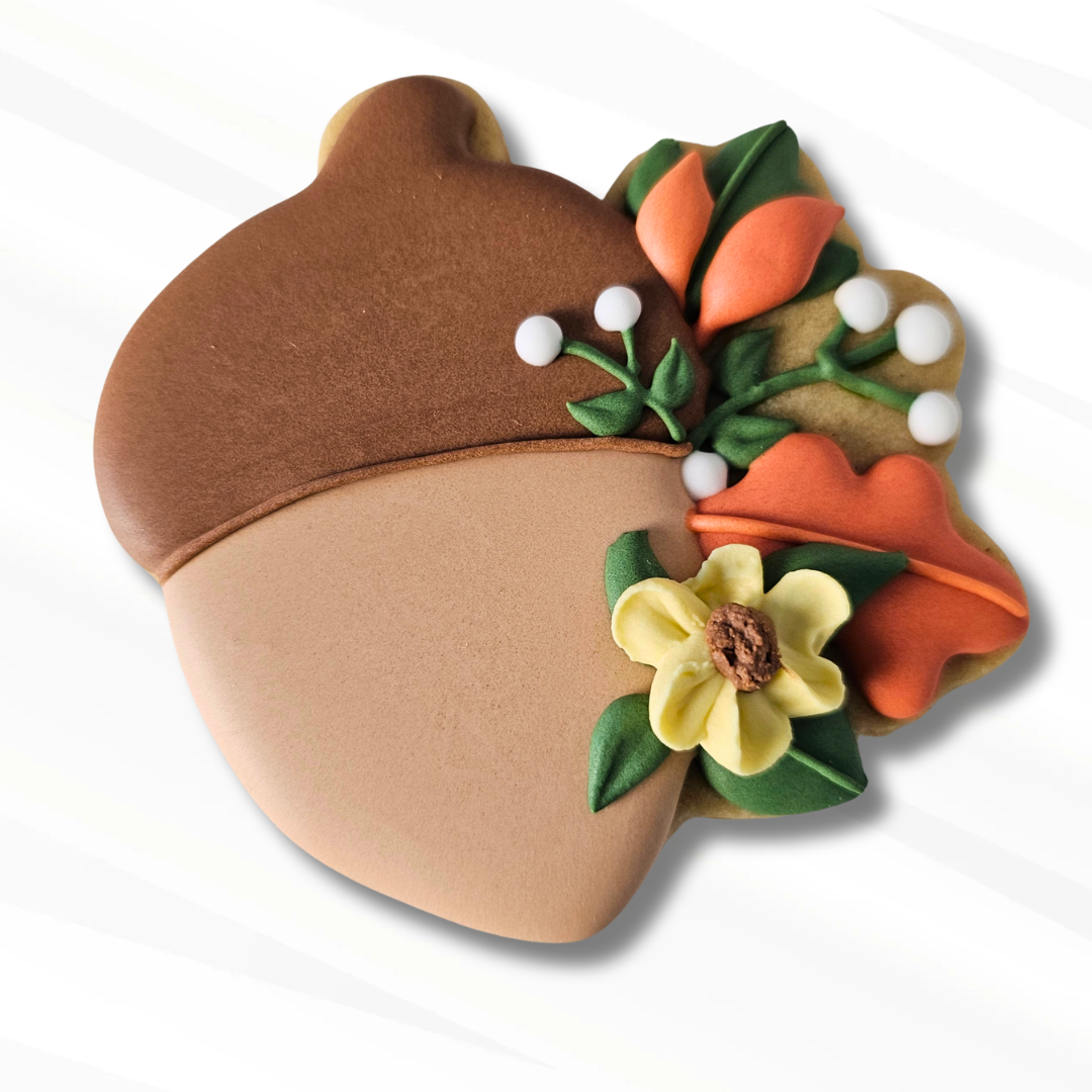 Decorated acorn sugar cookie with yellow royal icing flowers and fall leaves in orange and green on a white background 