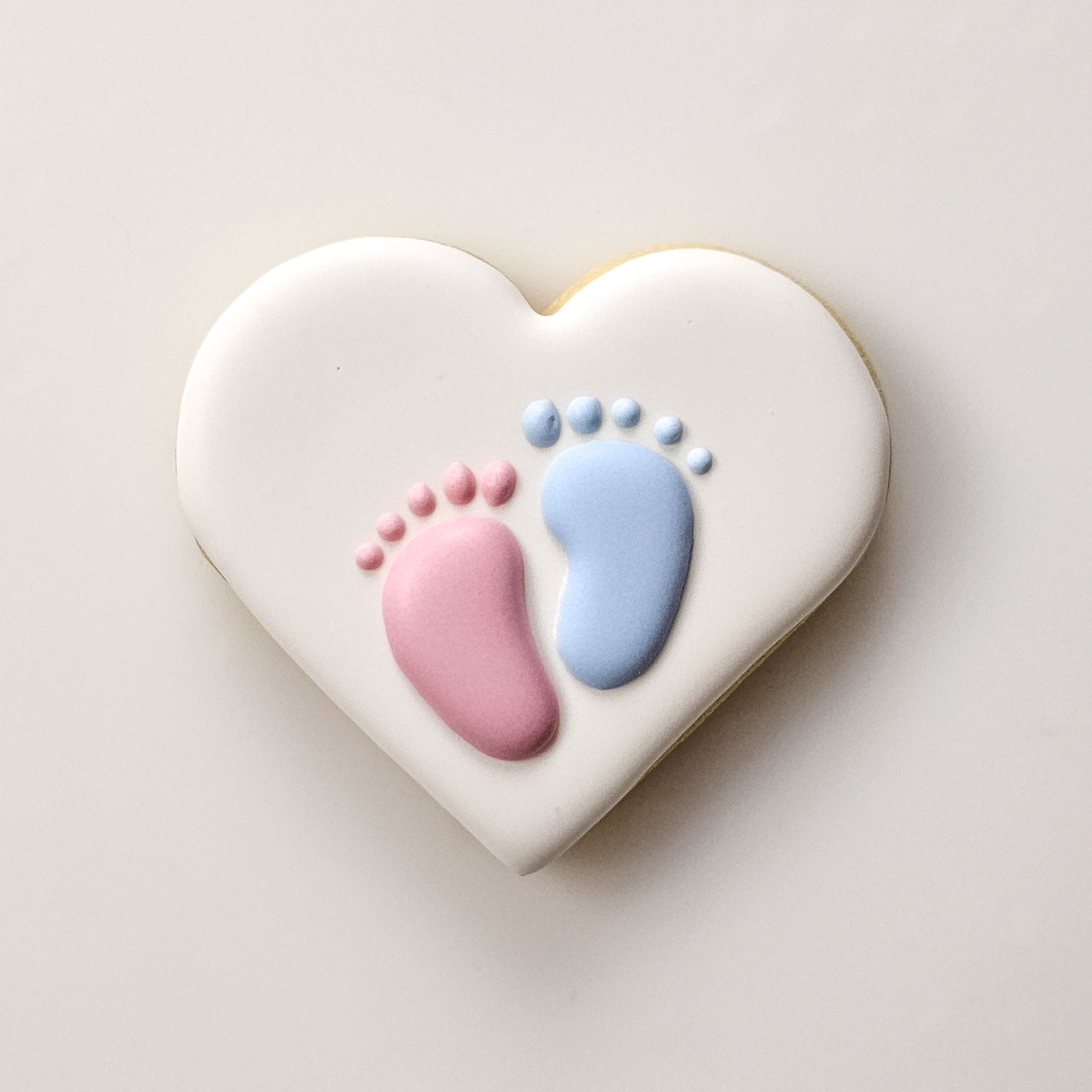 Heart-shaped sugar cookie with pink and blue baby footprints 