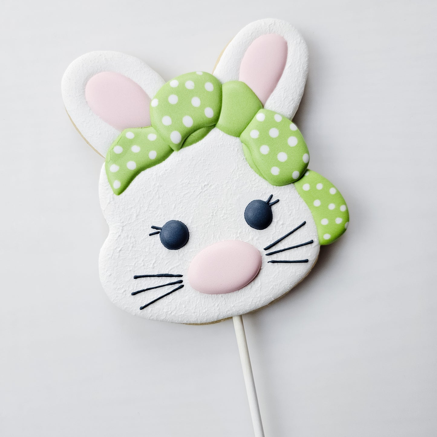 Decorative girl bunny cookie on a stick with a green bow against a light background