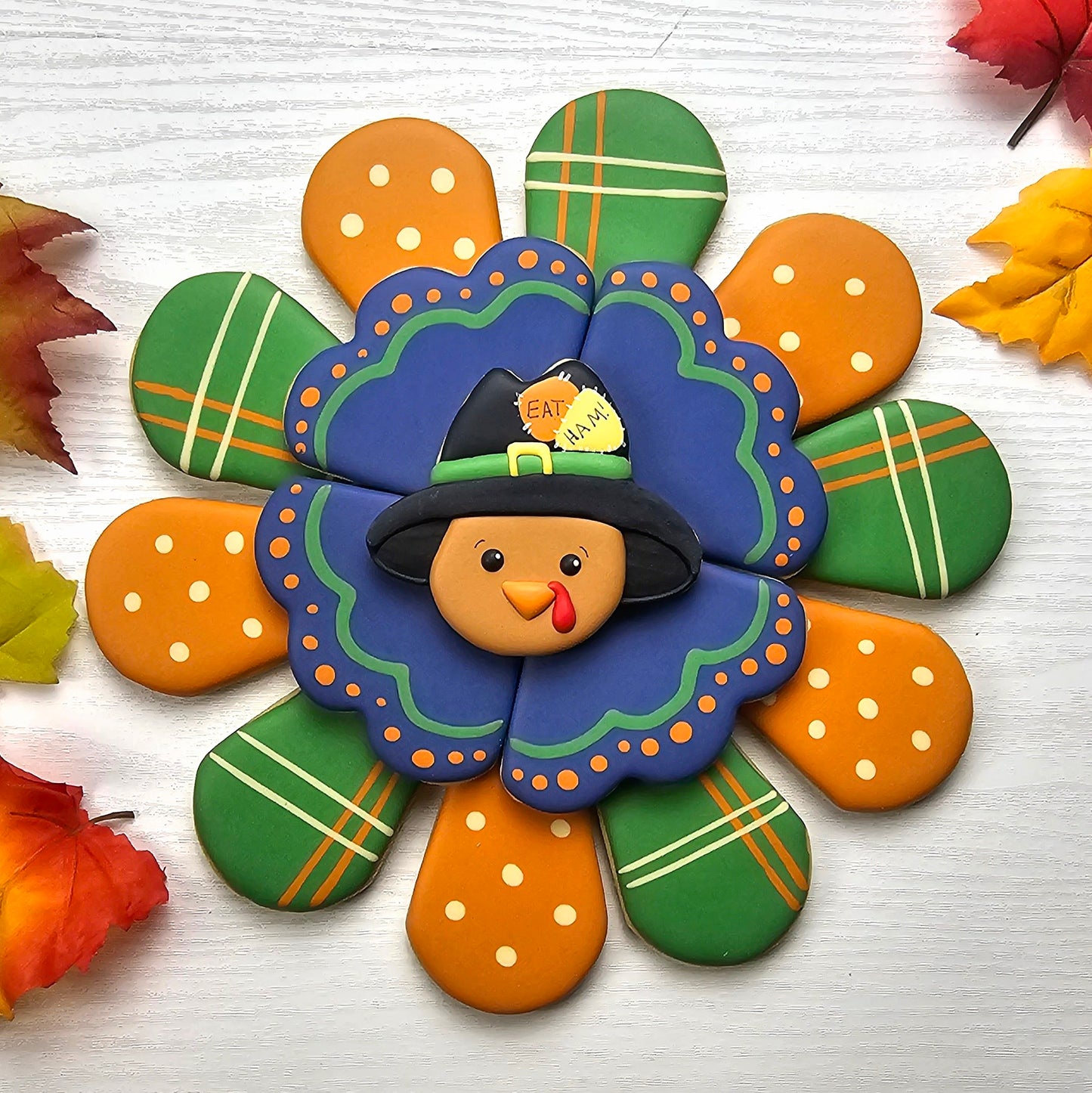 Decorative Thanksgiving sugar cookie platter with a center cookie shaped like a turkey with a hat on a white background with autumn leaves.