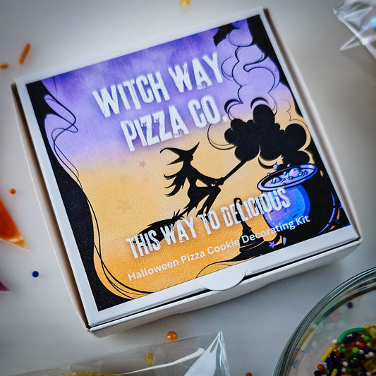 A small cookie pizza box featuring a Halloween-themed illustration with the text 'Witch Way Pizza Co.' and 'This Way to Delicious,' labeled as a Halloween Pizza Cooking Decorating Kit.