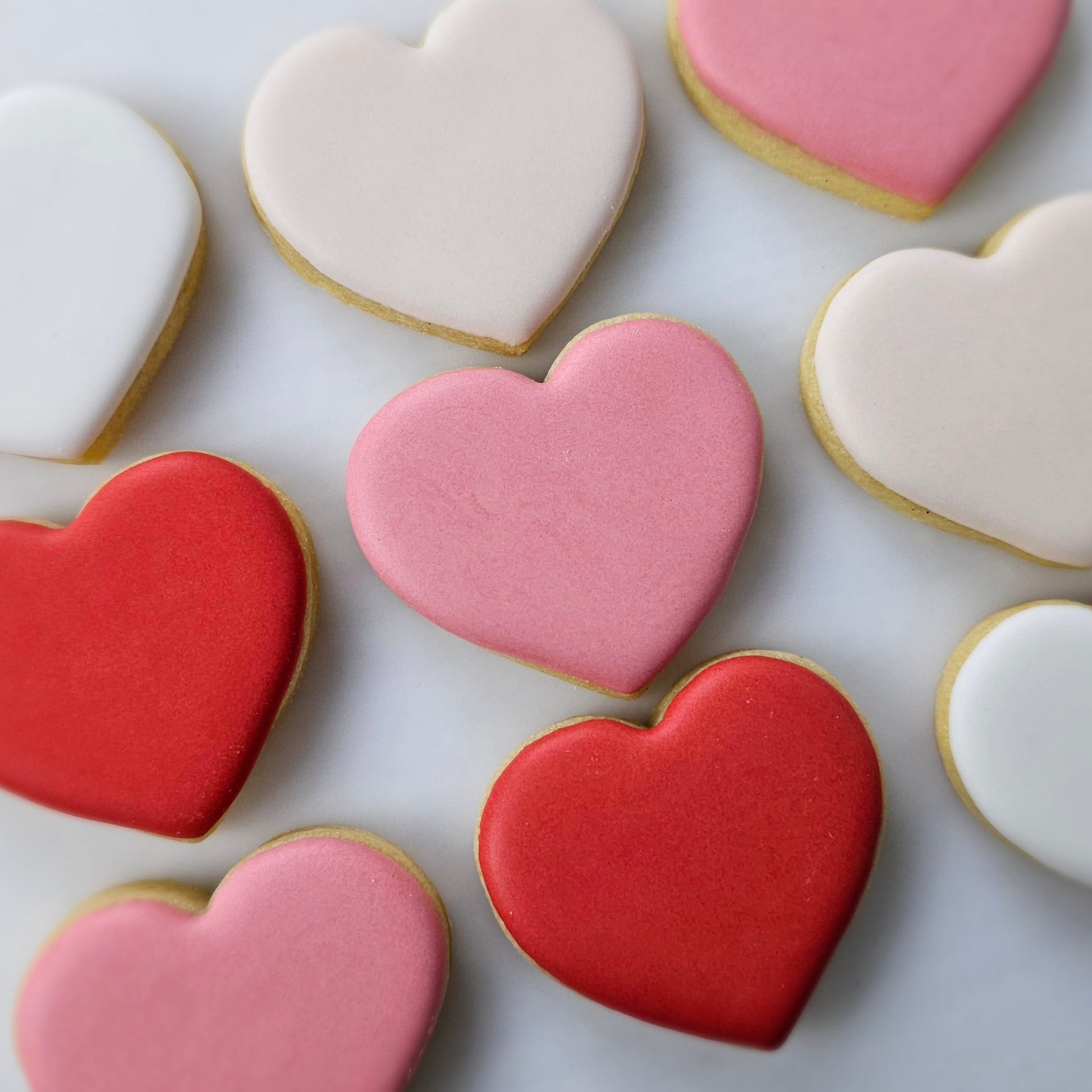 Heart-shaped cookies in red, pink, and white on a light gray background