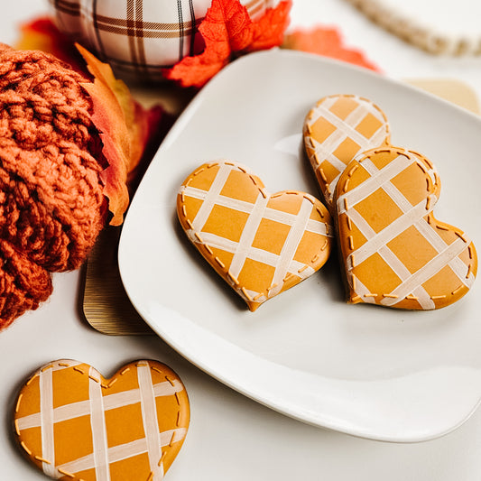 Heart-shaped cookies with plaid design on a white plate, surrounded by autumn-themed decor.