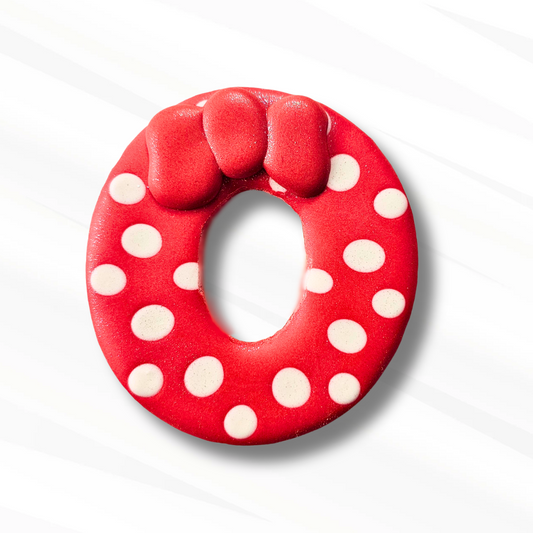 Letter O sugar cookie decorated in red royal icing with white polka dots and a red bow on top like Minnie Mouse