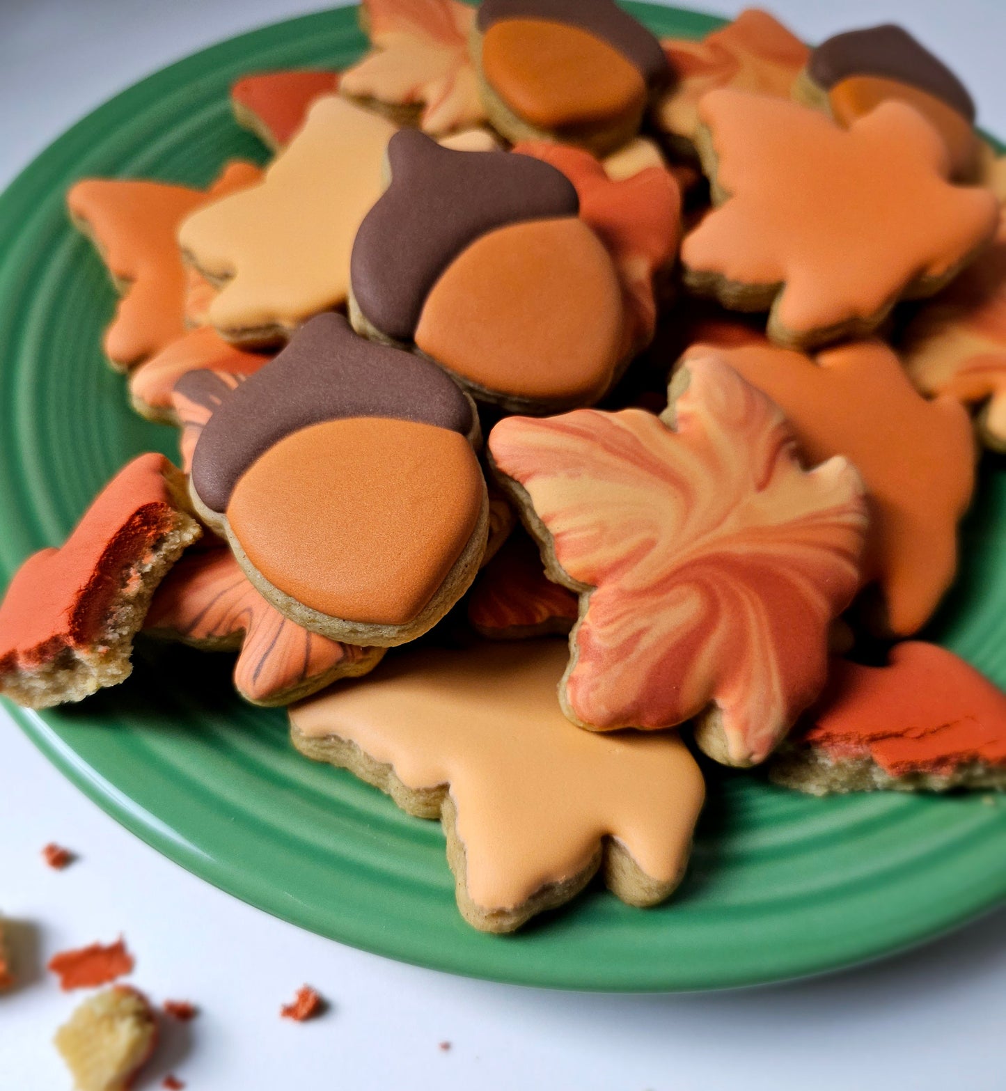 Collection of autumn-themed cookies shaped like leaves and acorns on a green plate.