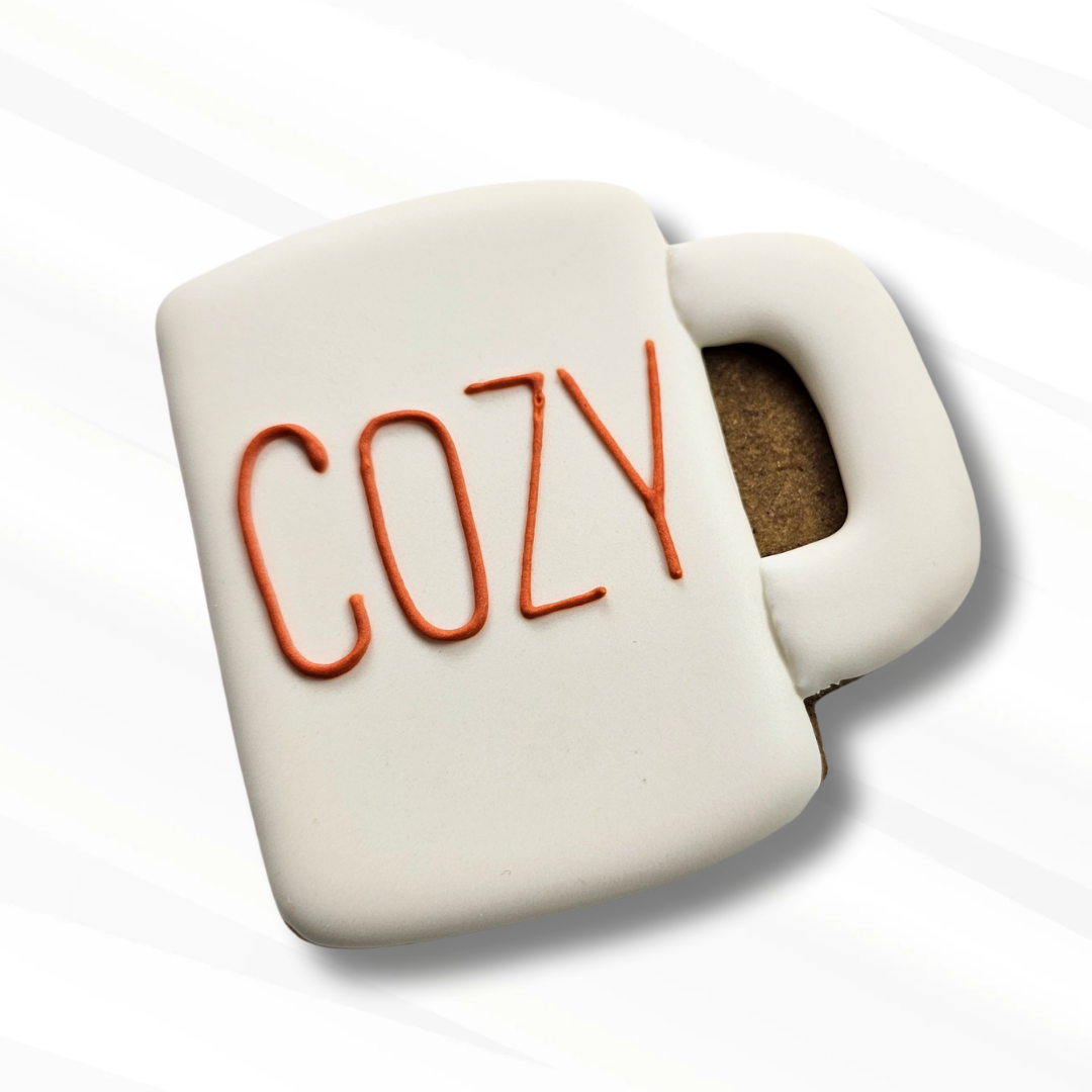 White mug-shaped sugar cookie with 'COZY' text on a white background
