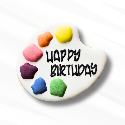 sugar cookie decorated like a paint palette that says happy birthday on a white background