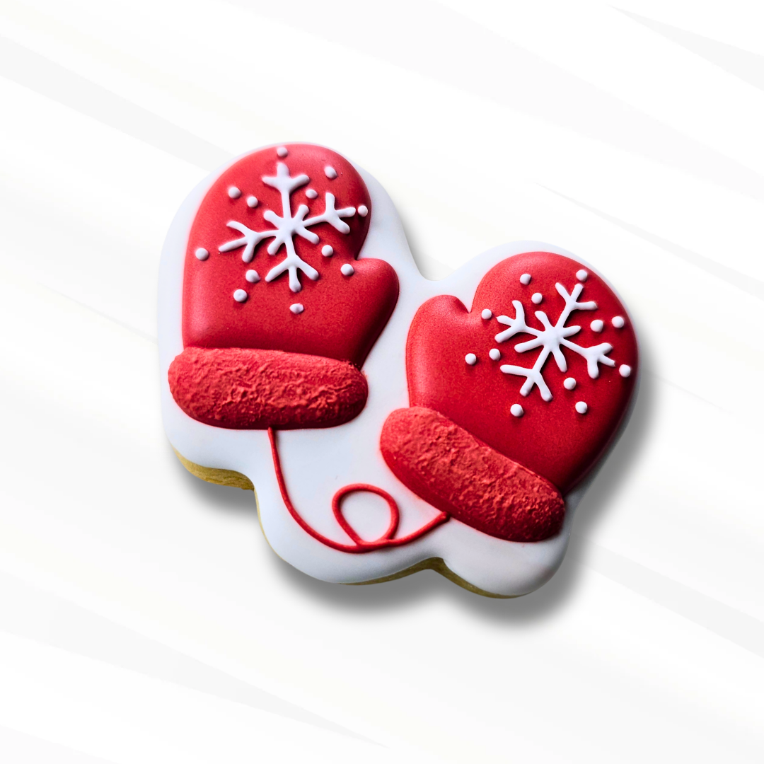 Decorative cookie shaped like red mittens with white snowflakes on a white background