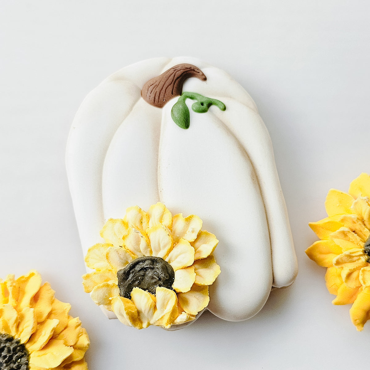 Tall pumpkin sugar cookie with white royal icing and a decorative yellow sunflower.