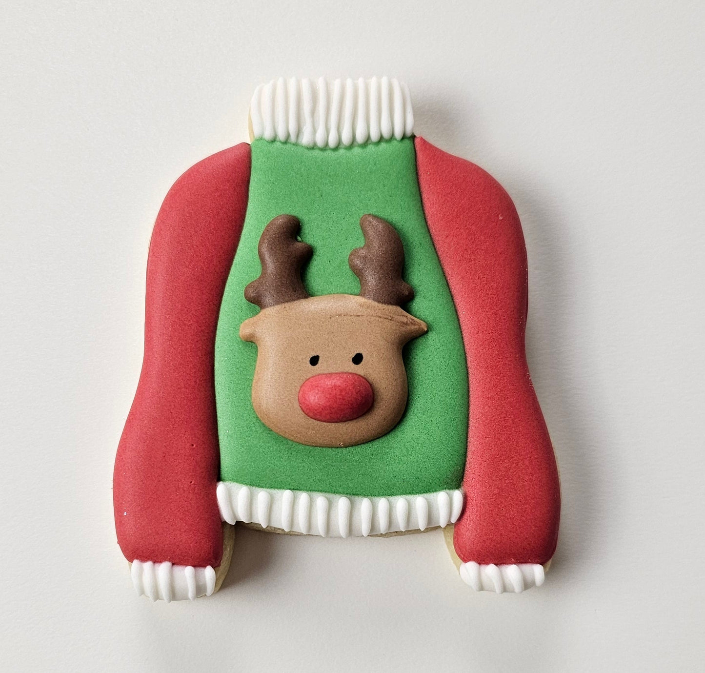Decorative Christmas cookie shaped like a ugly sweater with a reindeer on a white background