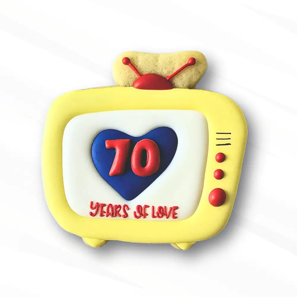 A sugar cookie decorated to look like a retro TV with a heart on the screen and '70 Years of love' piped over the heart using royal icing transfers for the numbers