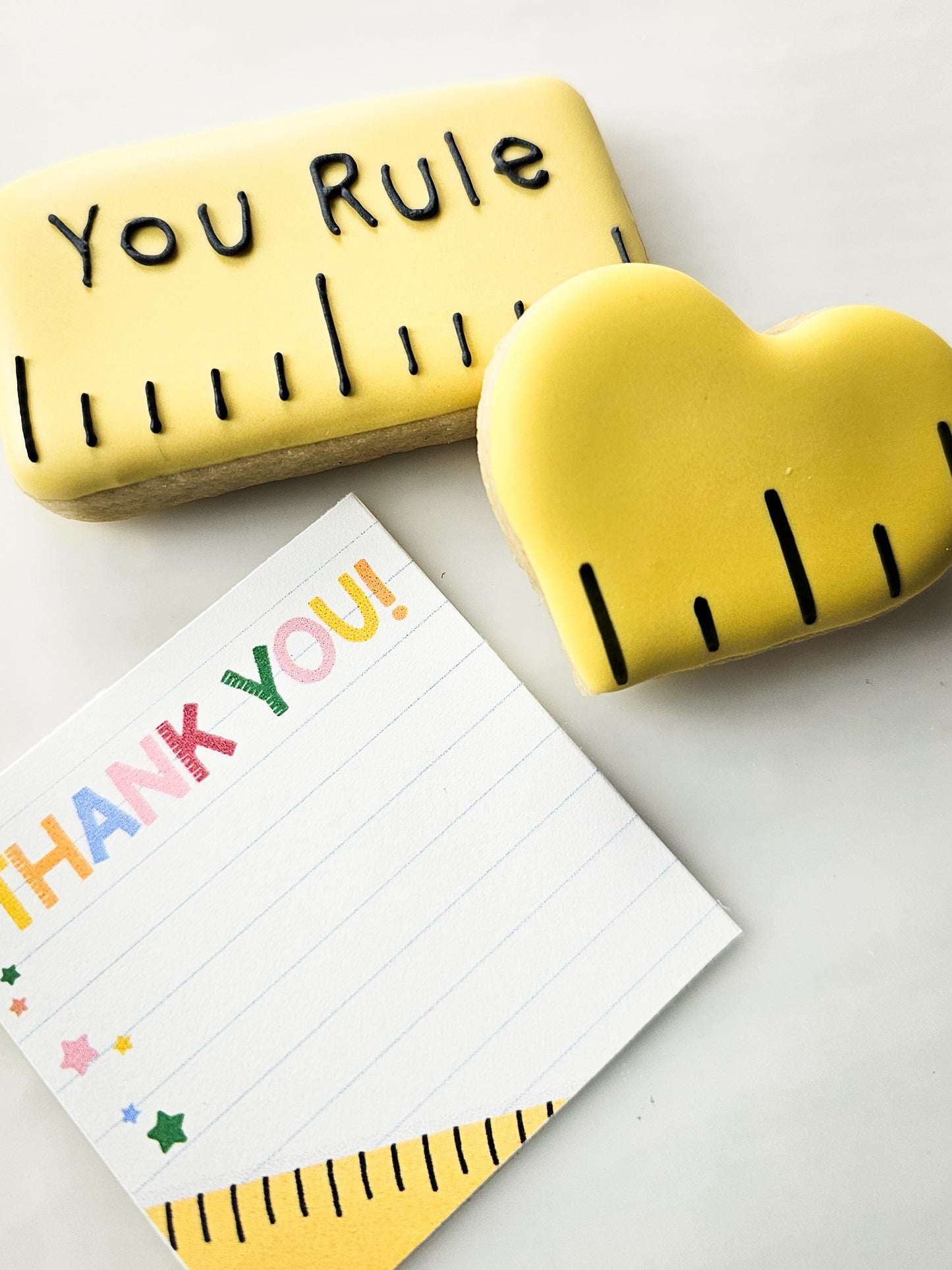 Yellow ruler-shaped sugar cookie with 'You Rule' text, heart-shaped ruler sugar cookie, and a 'Thank You!' tag on a white background