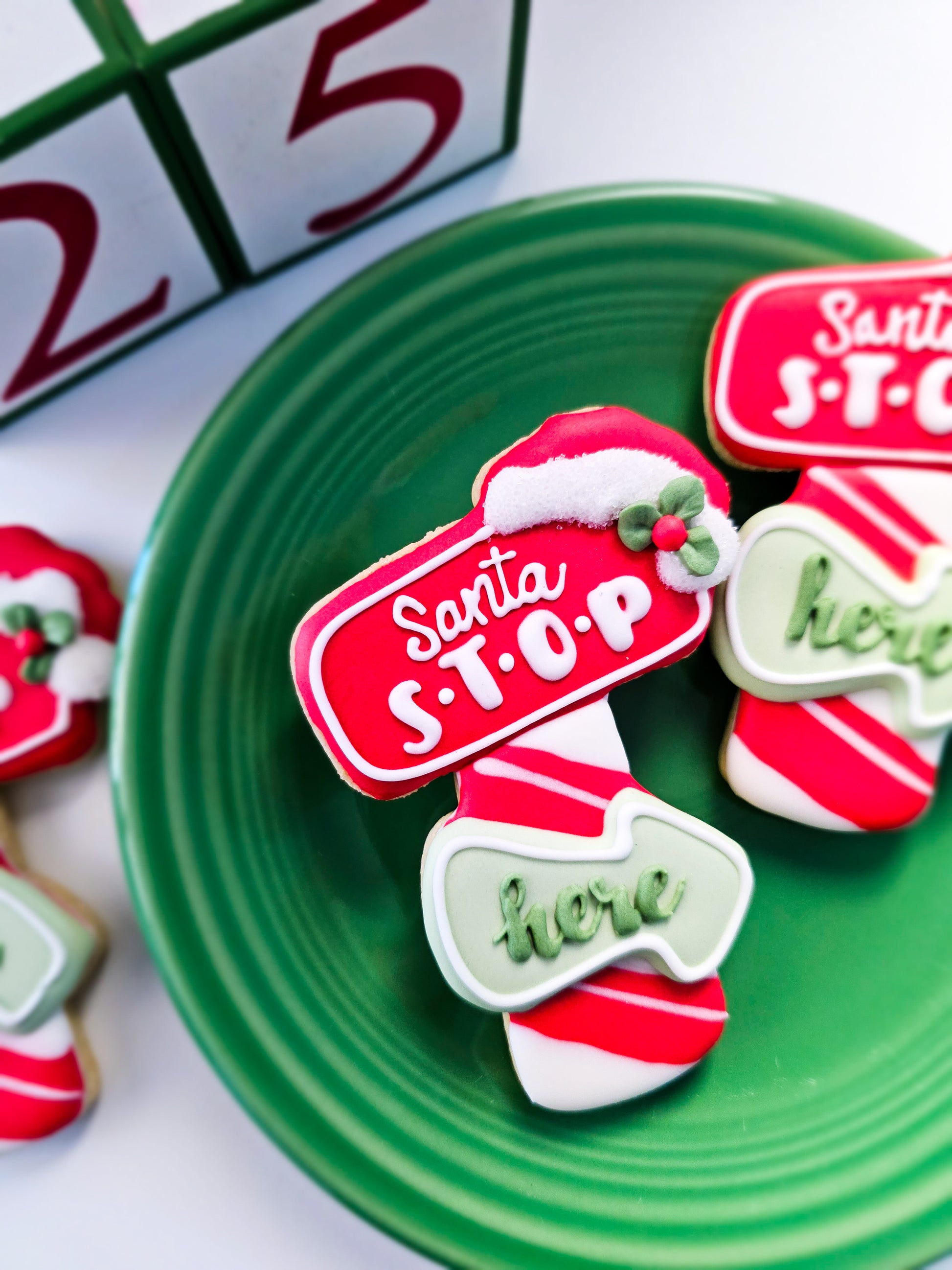 Santa Stop Here decorated sugar cookies arranged on a green plate with wooden calendar blocks visible in the background
