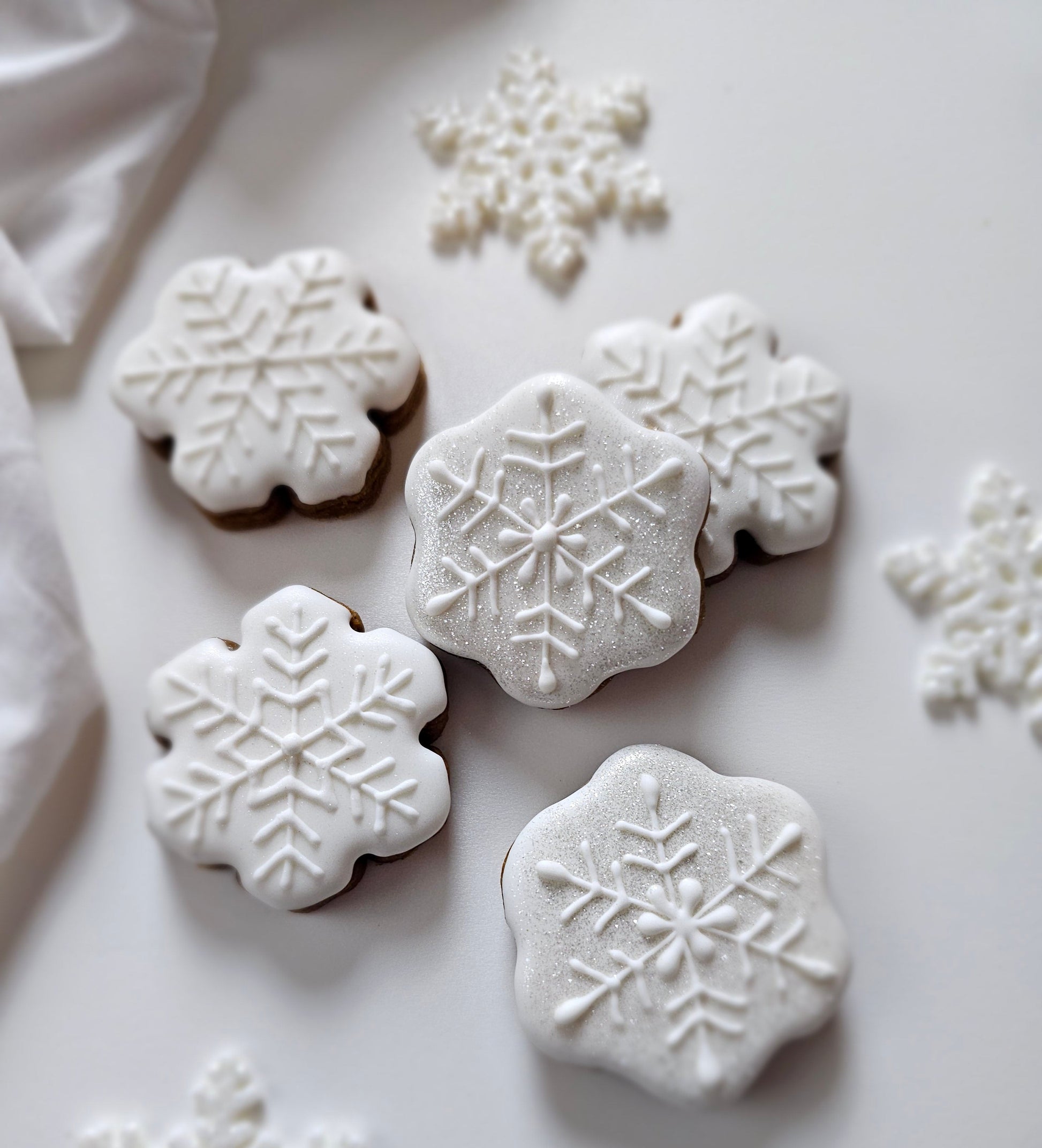 White snowflake sugar cookies on a white plate with decorative snowflakes around.