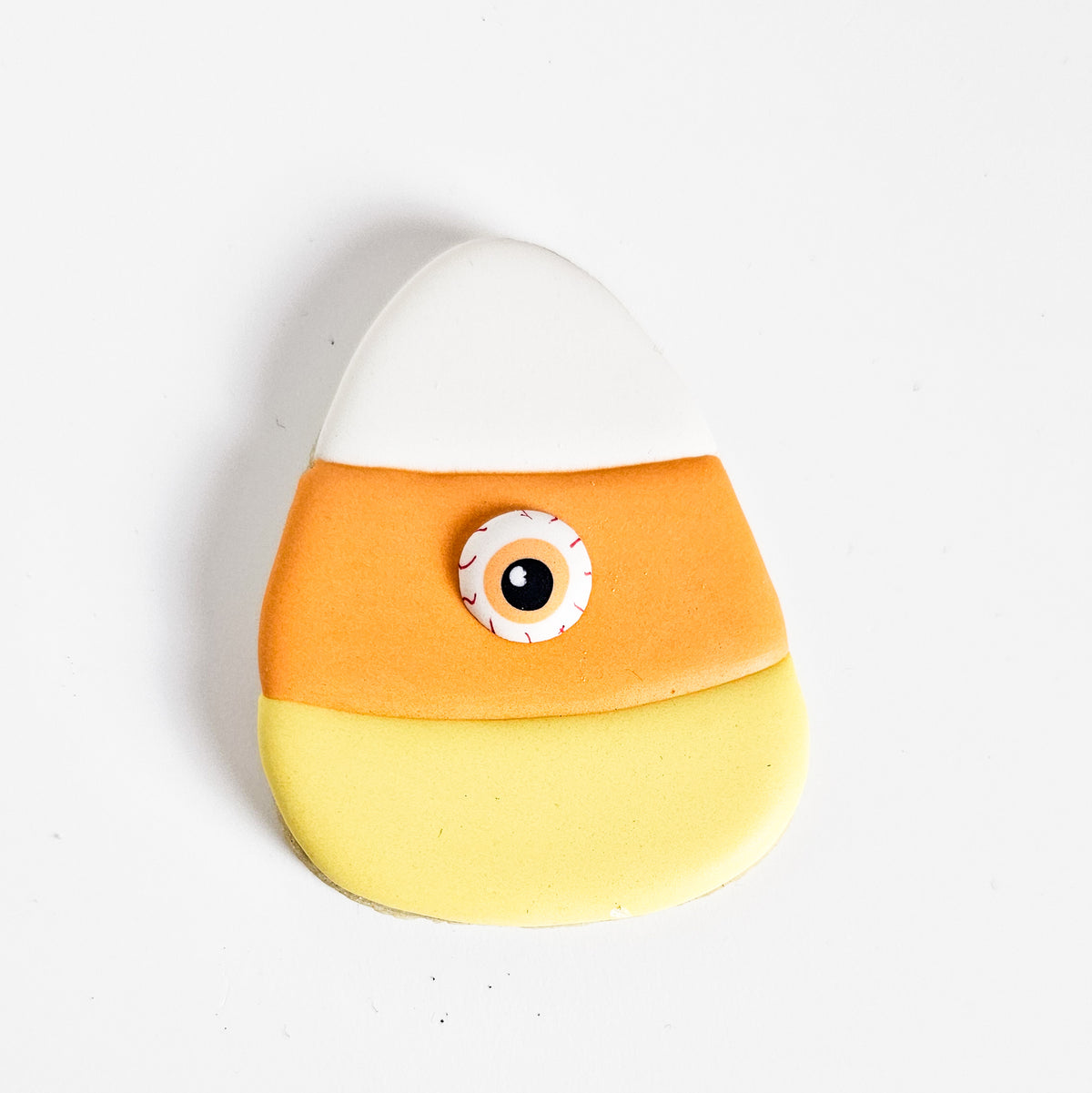 Candy corn monster sugar cookie decorated with a bloodshot eyeball royal icing transfer