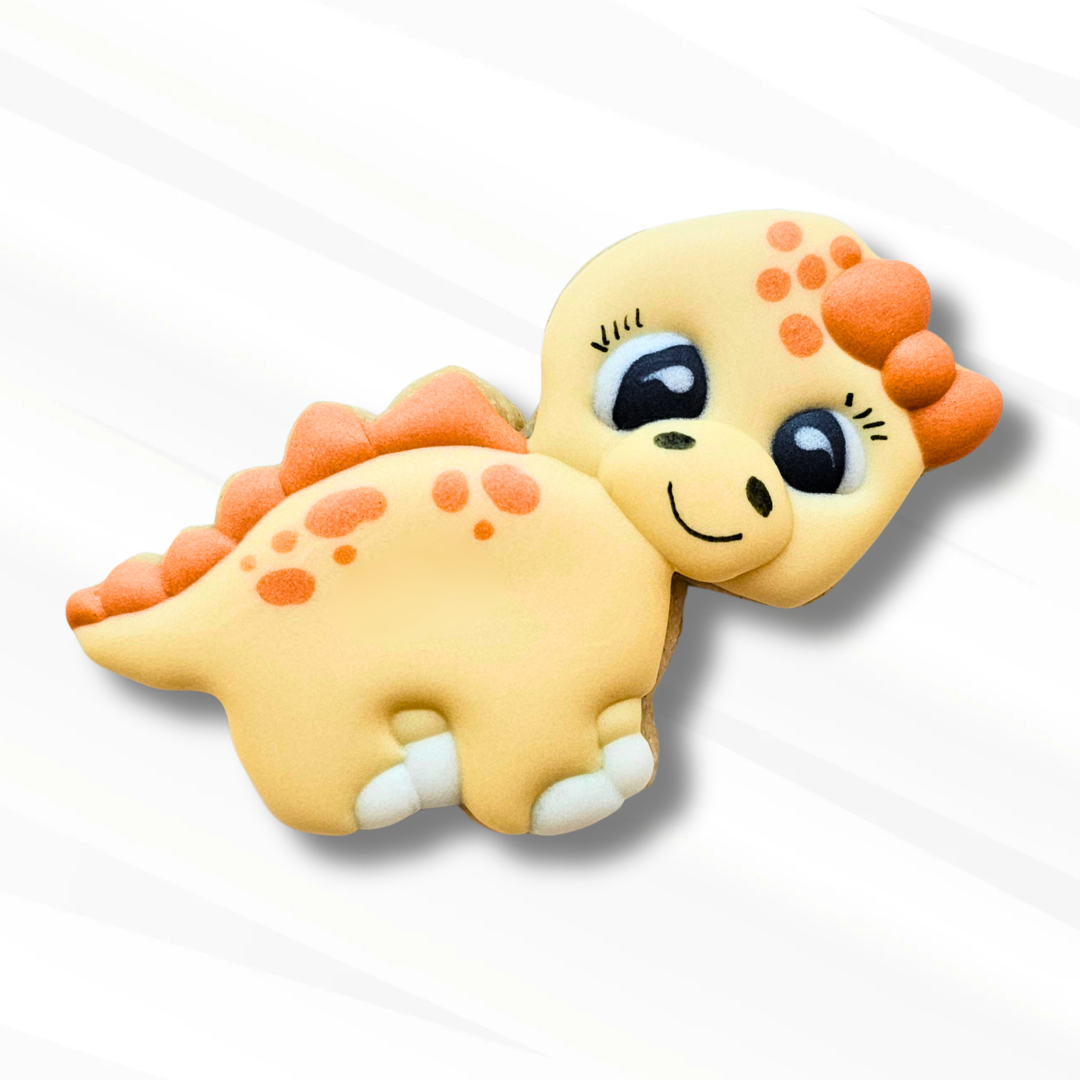 A cute, cartoon-style stegosaurus dinosaur sugar cookie in pale yellow with orange spots and spikes, and large black eyes shown on a white background with a soft drop shadow