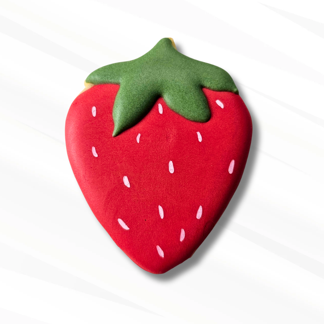 A strawberry-shaped sugar cookie decorated with bright red icing and a green icing top, shown on a light gray background with soft diagonal shadows.