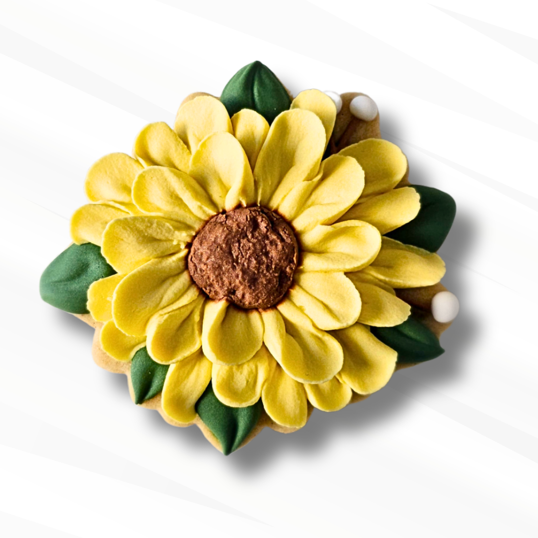 A sunflower-shaped sugar cookie in bright yellow, with a brown textured center and green leaf accents, shown on a white background with a soft shadow.