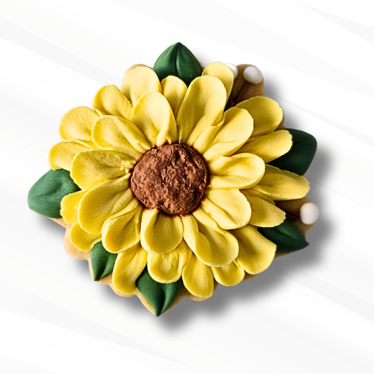 A sunflower-shaped sugar cookie in bright yellow, with a brown textured center and green leaf accents, shown on a white background with a soft shadow.