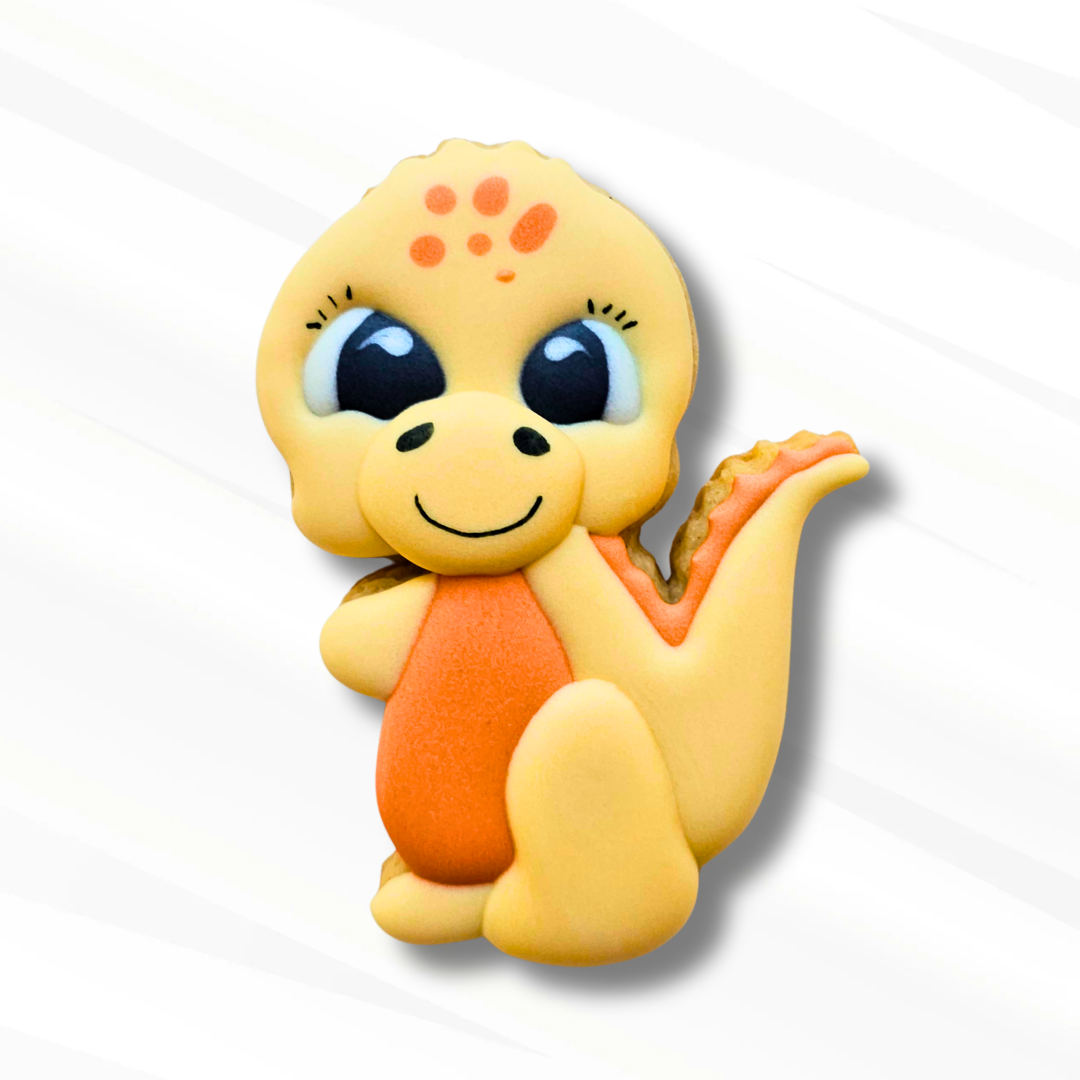 A cute, stylized cartoon dinosaur sugar cookie in pale yellow with orange accents, large eyes, and a black smile, shown on a white background with a soft shadow.